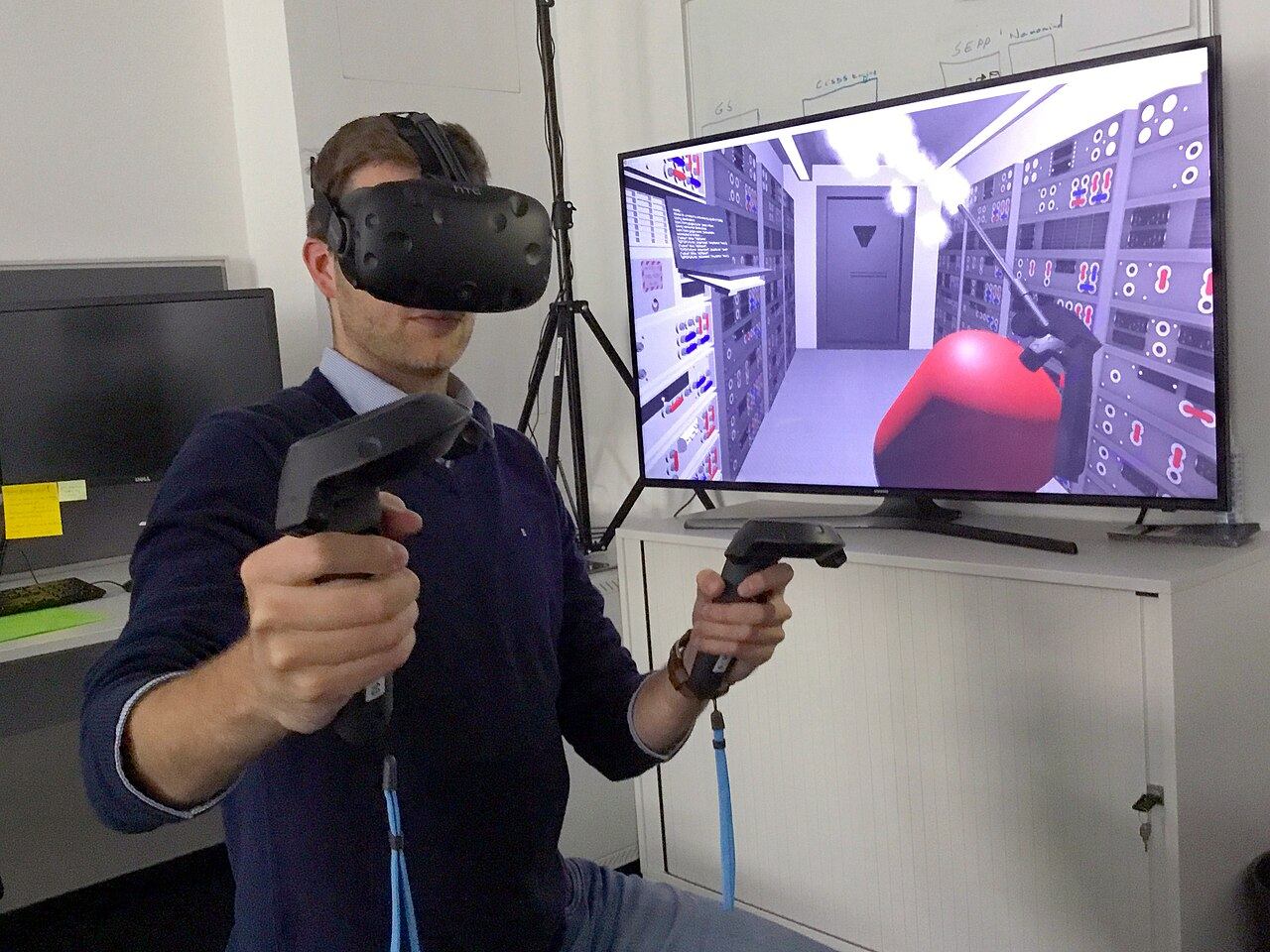 Чоловік у VR-шоломі з контролерами перед екраном з картинкою з гри