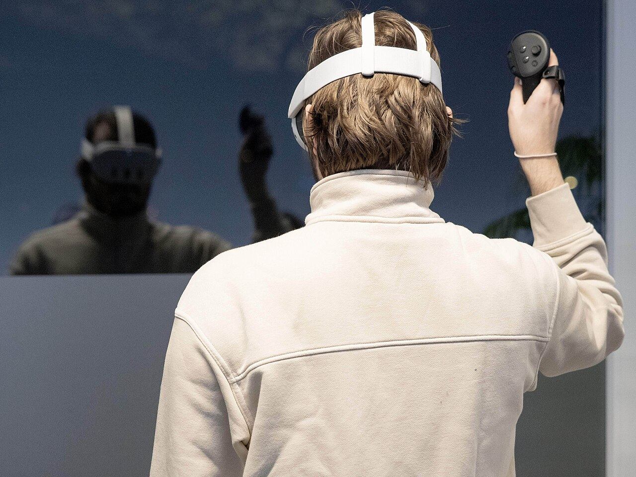 Гравець у VR-шоломі з контролерами в обох руках, вигляд ззаду